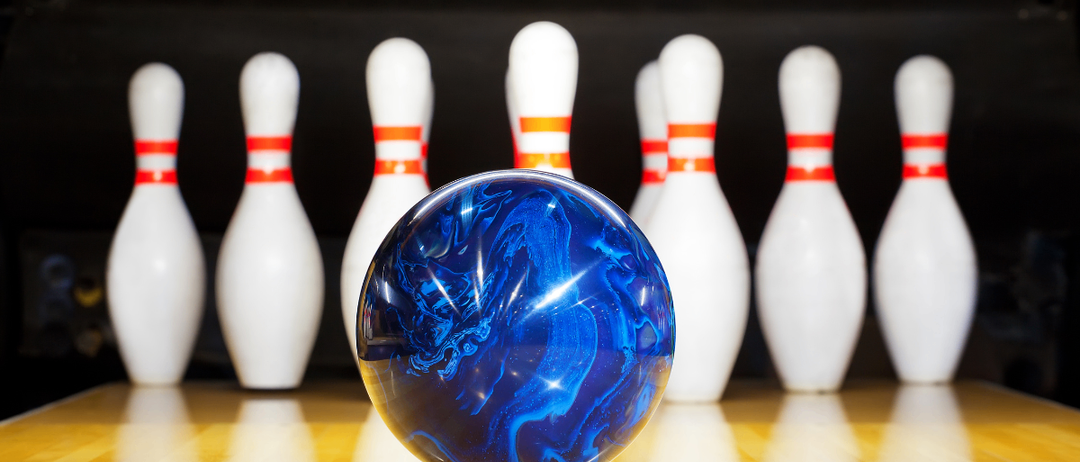 Eine blaue Bowlingkugel vor einer Reihe weißer Bowlingkegel mit orangefarbenen Bändern.