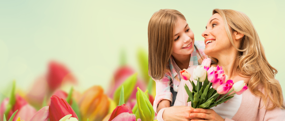 Eine Mutter und Tochter stehen in einem Feld bunter Tulpen und lächeln sich an. Die Tochter hält einen Strauß rosa und weißer Tulpen.