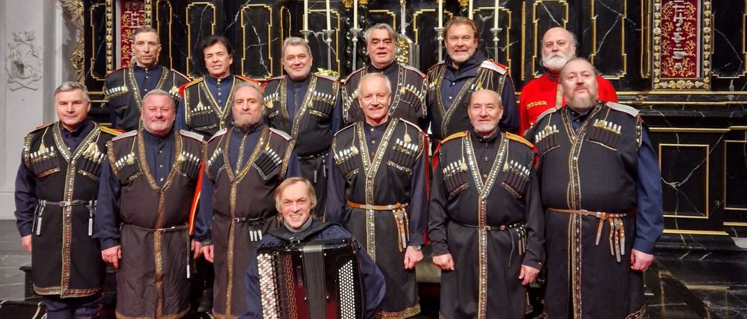 Ein Chor in traditioneller Kleidung, mit einem Mitglied, das ein Akkordeon spielt, posiert vor einem Kirchenaltar.
