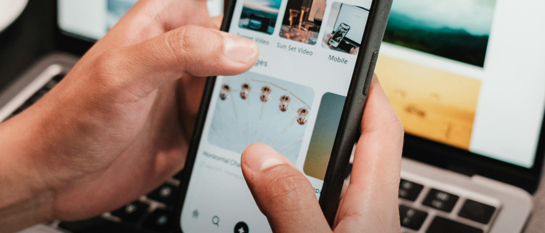 Eine Person hält ein Smartphone mit einem Bildschirm, der verschiedene Bilder und Text anzeigt, über einem Laptop mit einem gelben Kreis, der 'GIB DEIN WISSEN WEITER' besagt.