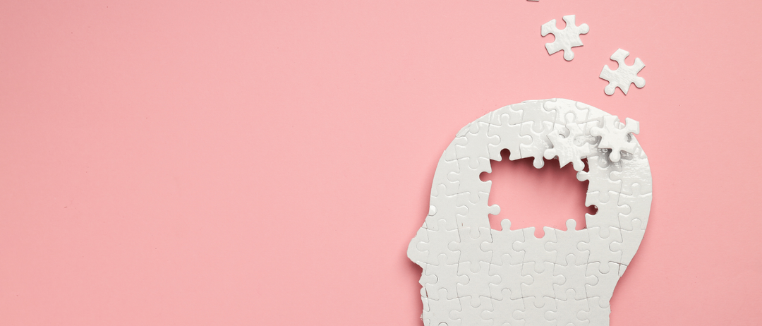 Ein weißer Puzzleteil in Form eines menschlichen Kopfes auf einem rosa Hintergrund mit anderen Puzzleteilen, die darüber schweben.