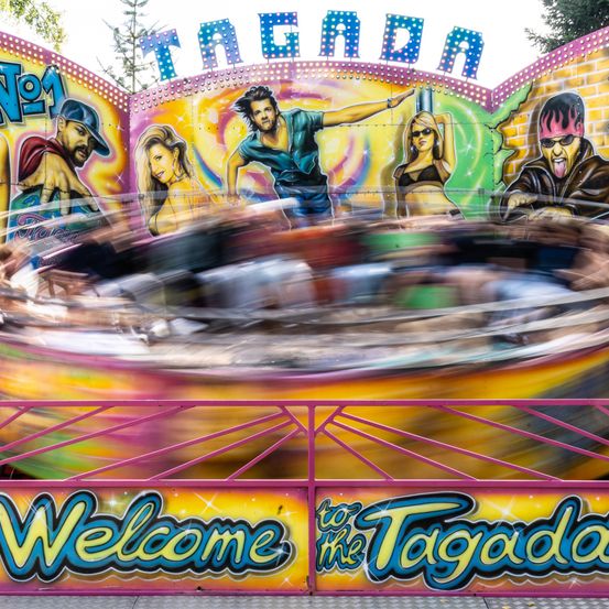 Eine farbenfrohe Vergnügungsfahrt namens Tagada, bemalt mit bunten Charakteren, dreht sich schnell mit Menschen im Inneren. Die Fahrt hat einen verwischten Bewegungseffekt.