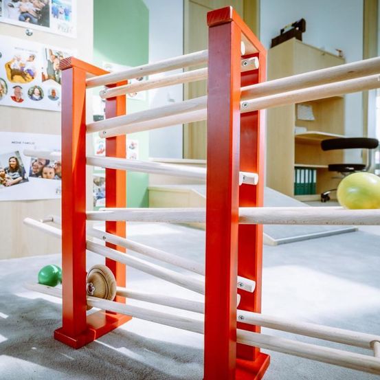 Ein bunter Spielbereich mit einer Holzstruktur und bunten Bällen. Die Wand hat Familienfotos und ein Kabinett mit einem gelben Ball oben.