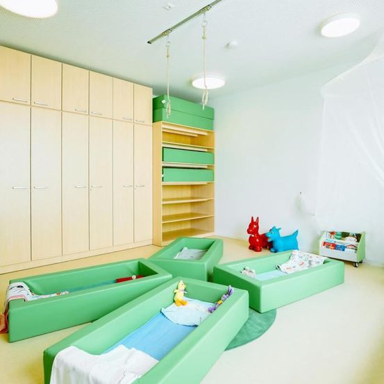 Ein Kinderzimmer mit grünen Krippen, Regalen, Schränken, Spielzeug und Spielzeug.