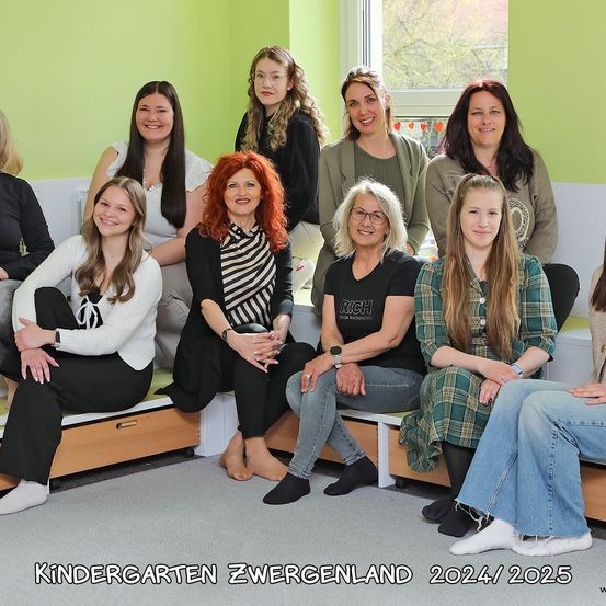Eine Gruppe von Frauen, lächelnd und sitzend, in verschiedenen Kleidungsstücken, vor einer grünen Wand mit Fenster. Der Text 'KINDERGARTEN ZWERGENLAND 2024/2025' befindet sich unten.