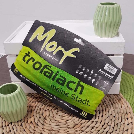 Ein Morf TROFAIACH-Paket in Grün und Schwarz liegt auf einem Holztisch mit zwei grünen Vasen. Die Verpackung enthält Anweisungen zur Verwendung.