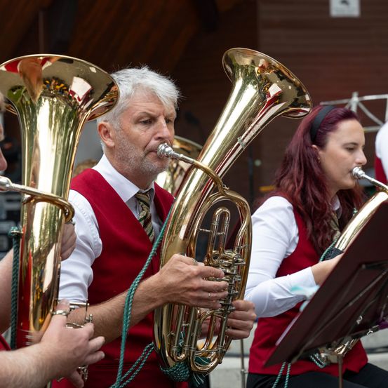 Ein Mann und eine Frau spielen Blechblasinstrumente in einer Band, möglicherweise bei einem Konzert.