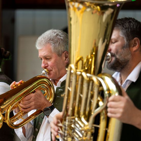 Ein Mann spielt Trompete und ein anderer Tuba, beide tragen grüne Westen.