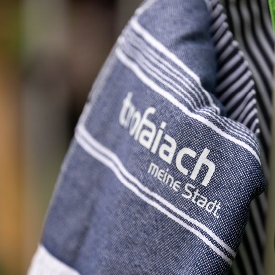 Ein Nahaufnahme eines blau-weiß gestreiften Shirts mit dem Aufdruck 'tofaiach meine Stadt'.