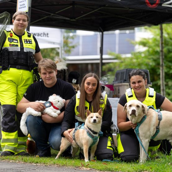Vier Personen in Sicherheitswesten posieren mit Hunden auf einer Rasenfläche, einer hält eine Katze.
