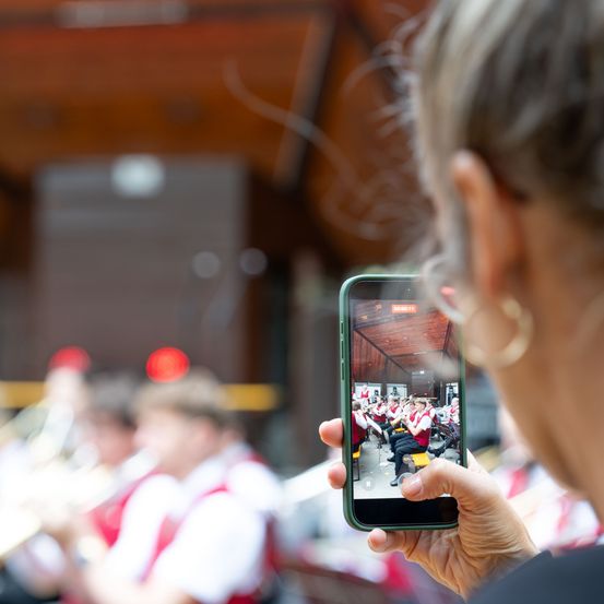 Eine Frau macht ein Foto von einer Band, die auf einer Bühne auftritt, mit einem Smartphone.