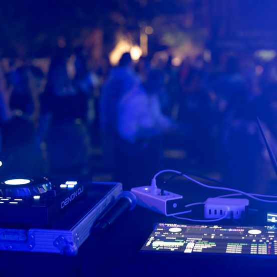 Ein DJ-Setup mit einem Plattenspieler und Mixer, beleuchtet von blauen Lichtern, mit einer Menge im Hintergrund.