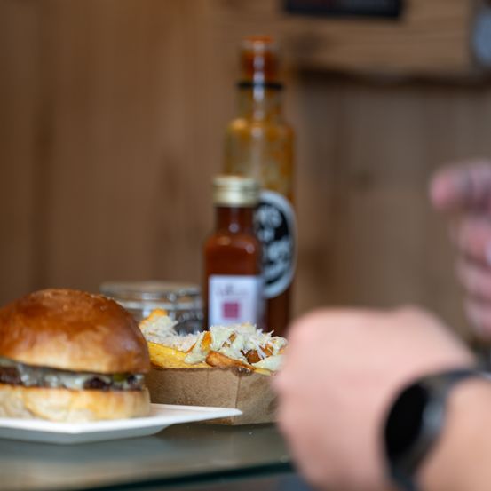 Ein Nahaufnahme eines Hamburgers auf einem weißen Teller mit Pommes und Gewürzen im Hintergrund.