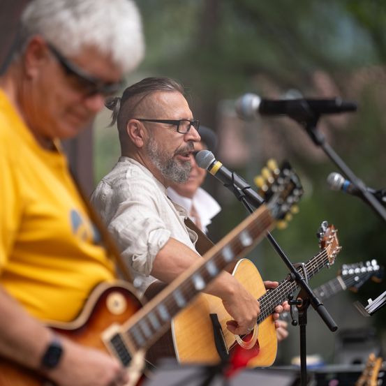 Zwei Männer spielen Gitarren auf der Bühne, einer singt in ein Mikrofon.