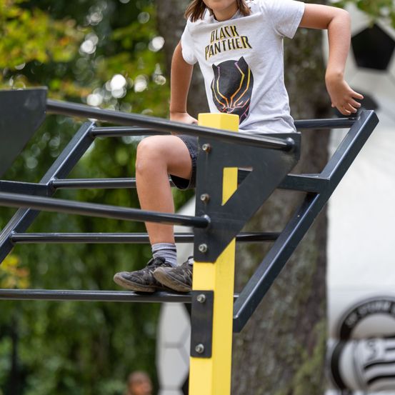 Ein junges Kind in einem Black Panther T-Shirt klettert auf einen gelben und schwarzen Kletterrahmen.