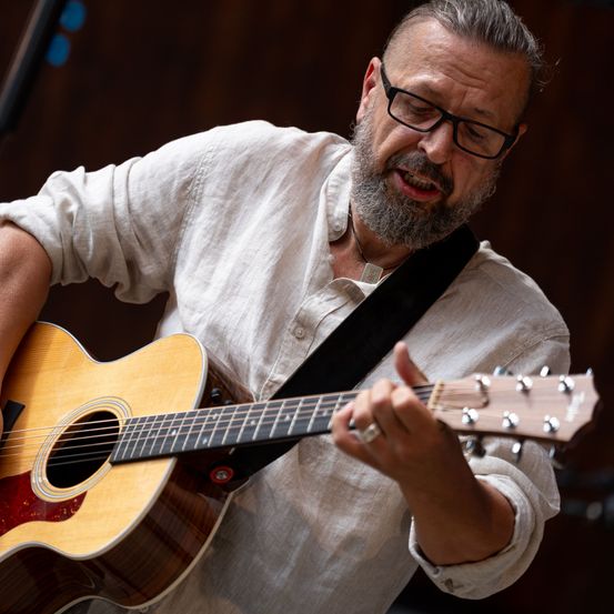 Ein Mann mit Bart und Brille spielt Gitarre, die Augen geschlossen und der Mund offen, vielleicht singt er.
