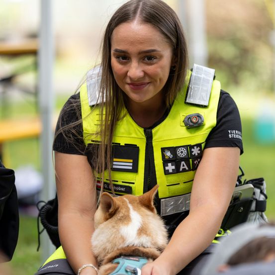 Eine Frau in einer gelben Weste mit reflektierenden Aufnähern und einem Hund auf dem Schoß.
