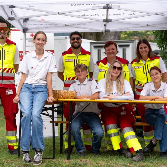 Eine Gruppe von Freiwilligen in Sicherheitswesten und Uniformen posiert für ein Foto unter einem Zelt.