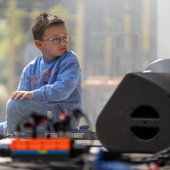 Ein junger Junge mit Brille sitzt auf dem Boden und konzentriert sich auf eine Musikproduktionseinrichtung.