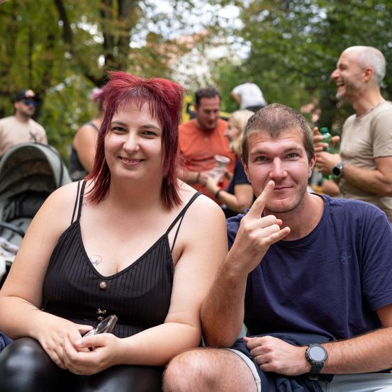 Eine Frau mit roten Haaren und ein Mann mit einer Uhr lächeln und posieren für ein Foto im Park.