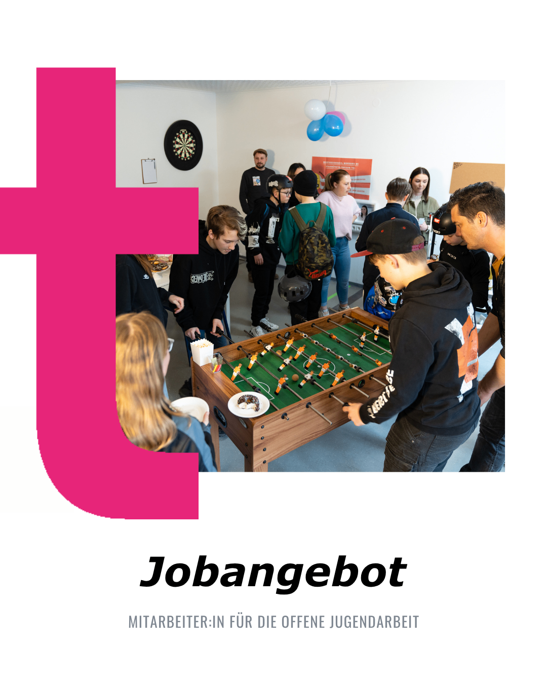 Menschen spielen Tischfußball in einem Raum mit einem Dartboard und Luftballons im Hintergrund.