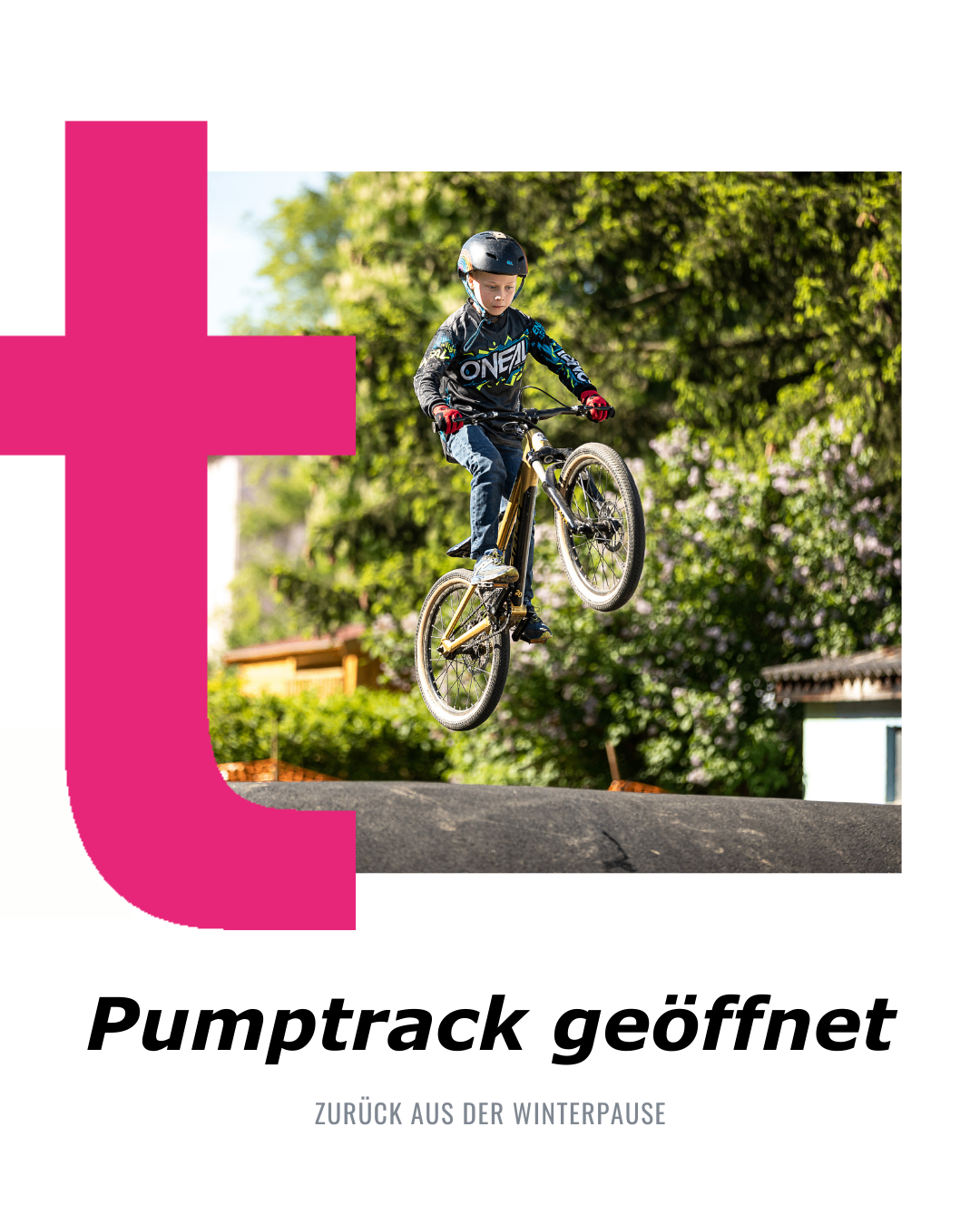Ein Junge mit Helm und Fahrradausrüstung fliegt mit seinem Fahrrad in der Luft über einem Pumptrack. Bäume und Häuser sind im Hintergrund.