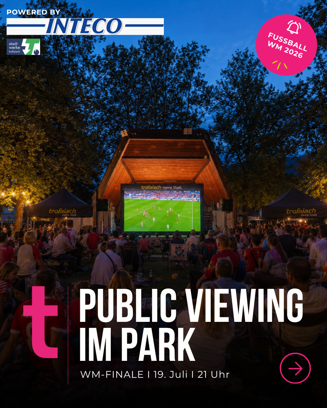 An outdoor event with a large screen showing a soccer match. People sit on chairs and tables in a park, with tents in the background.