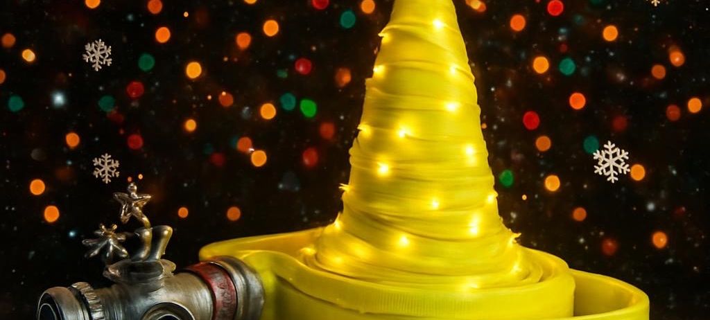 Ein gelber Weihnachtsbaum mit einem Stern auf der Spitze, dekoriert mit Lichtern, ruht auf einer roten Plattform. Daneben ist ein Feuerwehrhydrant ausgestellt. Schneeflocken schweben im Hintergrund.