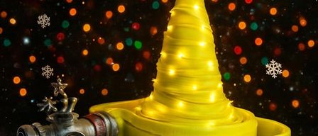 Ein gelber Weihnachtsbaum mit einem Stern auf der Spitze, dekoriert mit Lichtern, ruht auf einer roten Plattform. Daneben ist ein Feuerwehrhydrant ausgestellt. Schneeflocken schweben im Hintergrund.