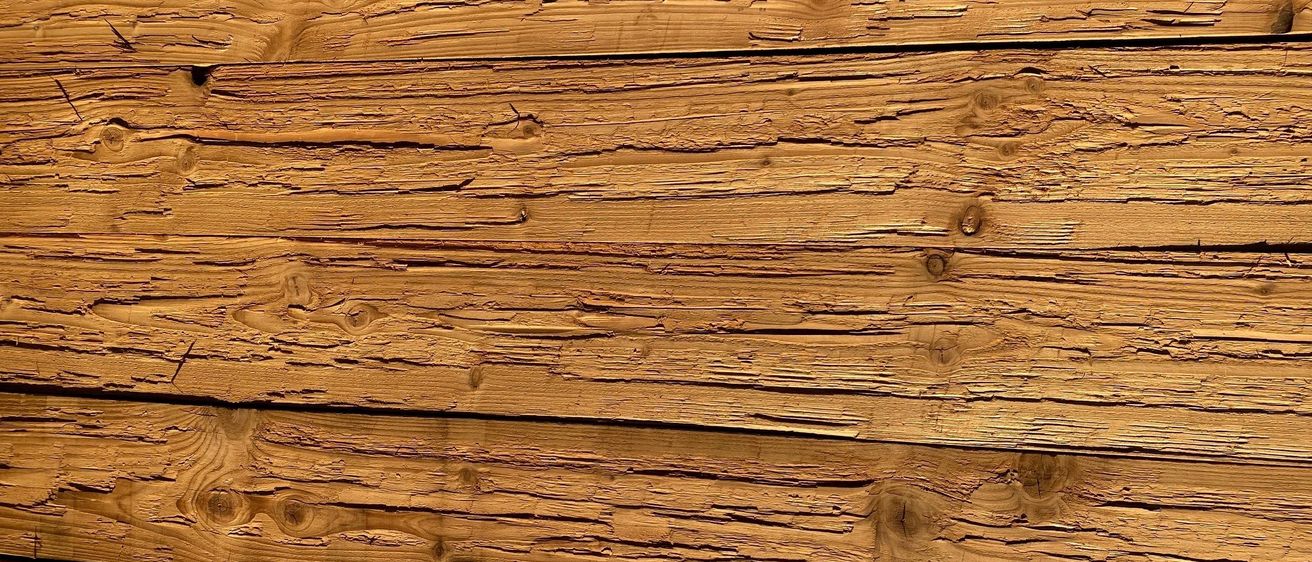 Eine Nahaufnahme von Holzbrettern mit sichtbaren Ästen und Maserungen. Das Holz hat einen verwitterten, rustikalen Look.