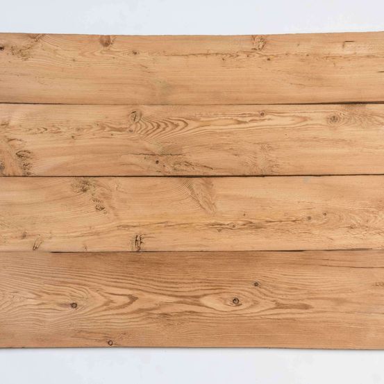 Eine Nahaufnahme von vier horizontalen Holzbrettern. Sie sind ordentlich angeordnet mit sichtbaren Holzmaserungen und Ästen. Das Holz sieht gealtert und verwittert aus.