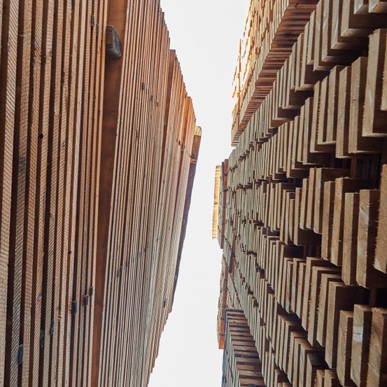 Ein Blick auf zwei Stapel von Holzbrettern, die in einem dreieckigen Muster gestapelt sind, ein Stapel erscheint höher mit mehr Schichten, vor einem hellen Himmel.