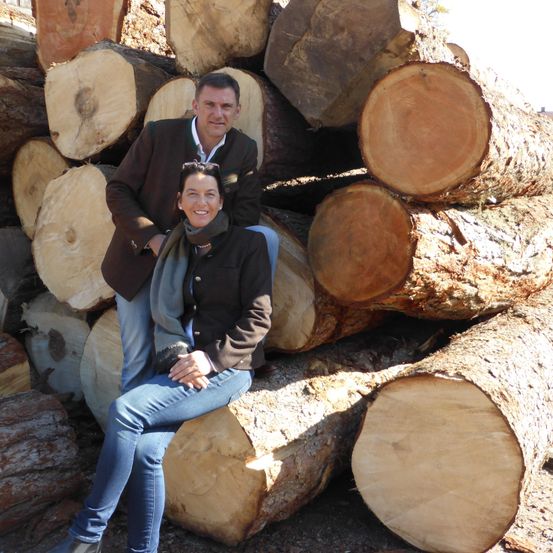 Ein Mann und eine Frau sitzen auf einem Stapel Holzscheite und lächeln für die Kamera.