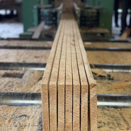 Eine Nahaufnahme einer Reihe von Holzbrettern auf einem Werkstattboden, mit einem Metallrahmen im Hintergrund.