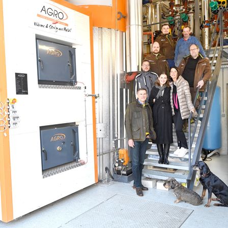 Eine Gruppe von Menschen steht auf einer Treppe, einige lächeln und posieren für ein Foto. Zwei Hunde sitzen auf dem Boden, einer schaut zur Kamera.