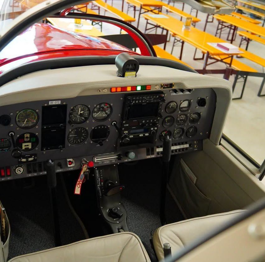 Das Innere eines kleinen Flugzeugs zeigt das Cockpit mit verschiedenen Anzeigen, Bedienelementen und einem roten und schwarzen Farbschema.