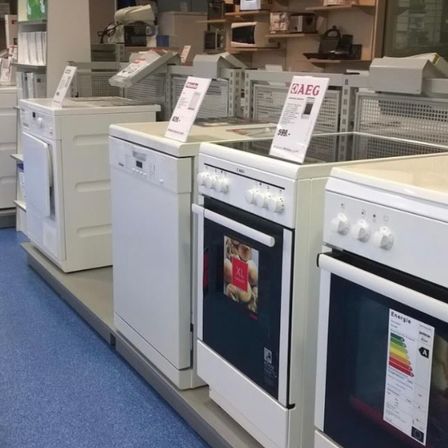 Ein Elektronikgeschäft zeigt mehrere weiße Geräte, darunter eine Waschmaschine, einen Geschirrspüler und Öfen, alle mit Preisschildern und Energieeffizienzetiketten.