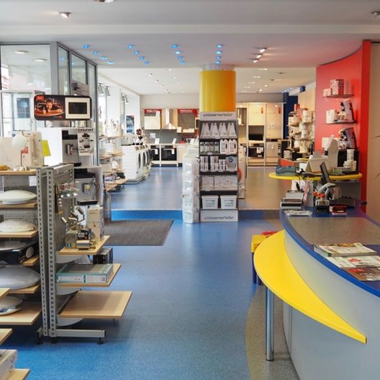 Das Innere eines Geschäfts mit blauem Boden, gelben Säulen und Regalen mit verschiedenen Produkten. Rechts befindet sich eine Theke mit Zeitschriften.