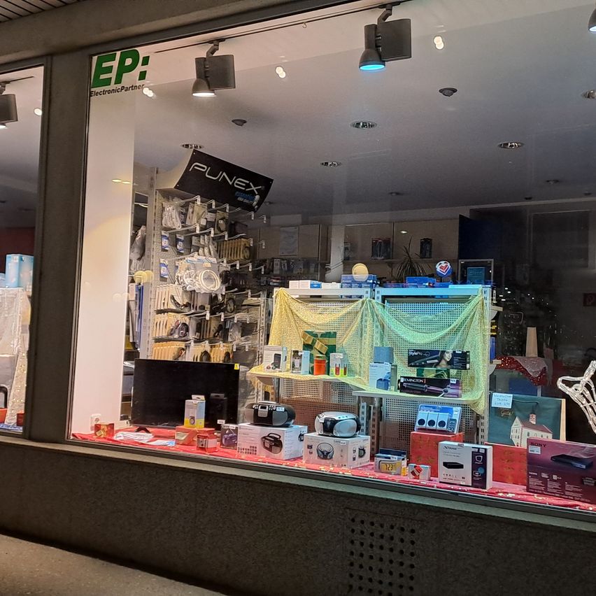 Ladenfenster mit Elektronikprodukten wie Monitor, Lautsprecher und Geschenkartikeln. Die Ausstellung hat einen roten Stoff mit mehreren Artikeln darauf und ein Schild mit der Aufschrift EP.