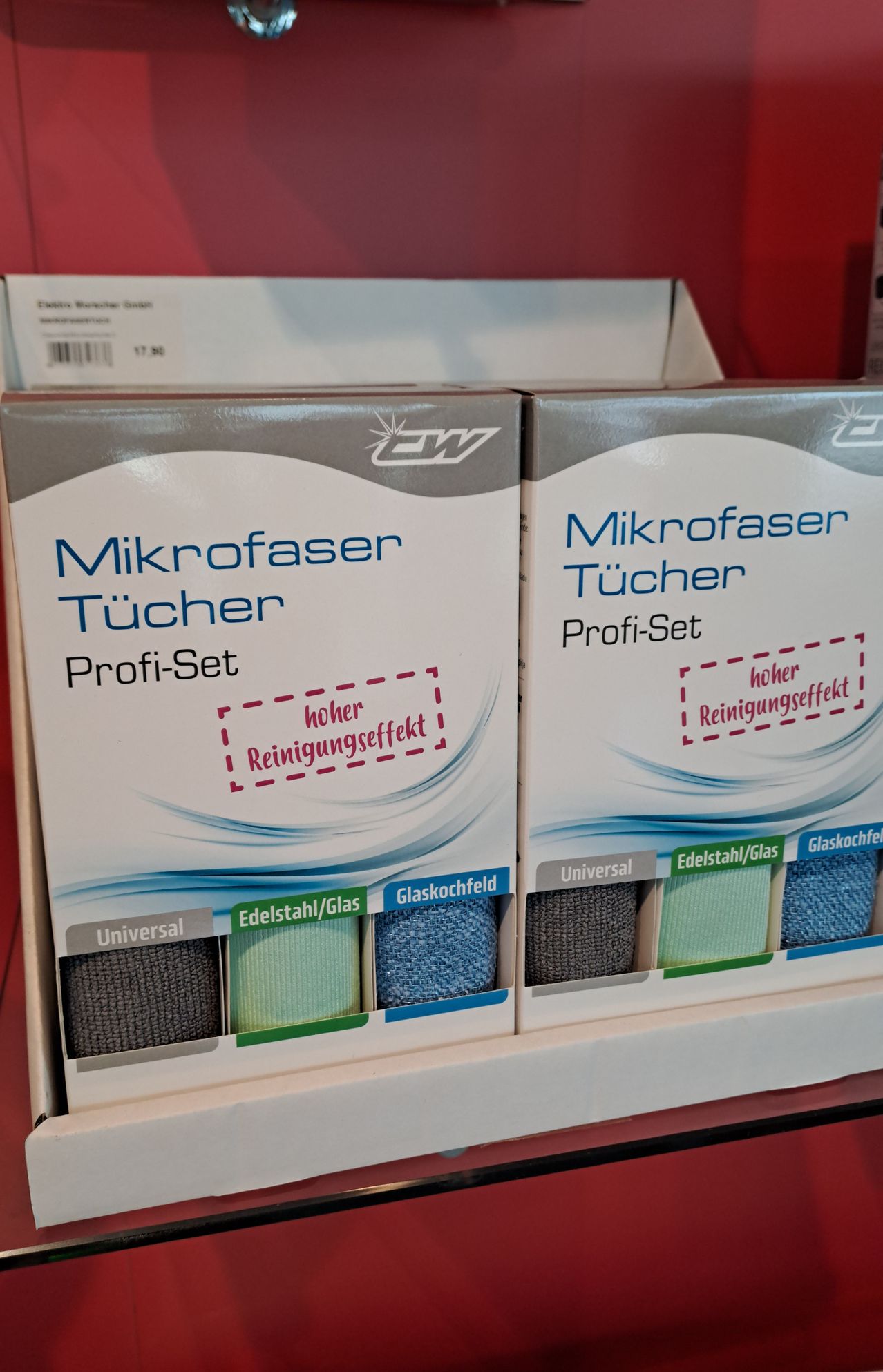 Zwei Schachteln Mikrofaser Tücher Profi-Set sind auf einem Regal ausgestellt. Jede Schachtel enthält verschiedenfarbige Mikrofasertücher für verschiedene Oberflächen. Die Schachteln sind mit 'Universal', 'Edelstahl/Glas' und 'Glaskochfeld' beschriftet.