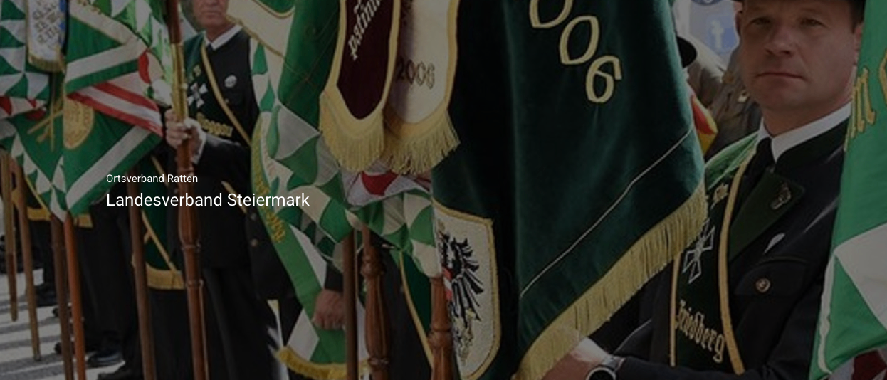 Uniformierte Personen stehen mit Flaggen und Bannern bei einer zeremoniellen Veranstaltung, die Fahne trägt 'und Steiermark.'