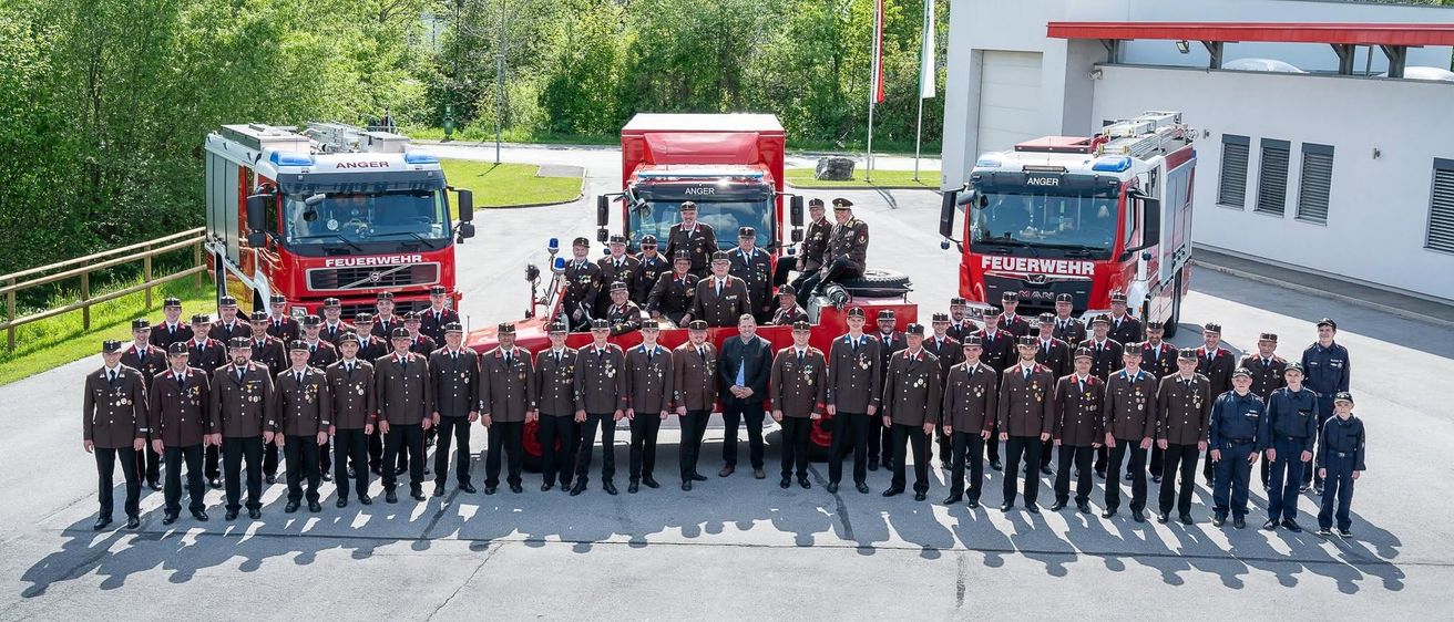 Eine Gruppe Feuerwehrleute in Uniform posiert für ein Foto vor zwei Feuerwehrautos.