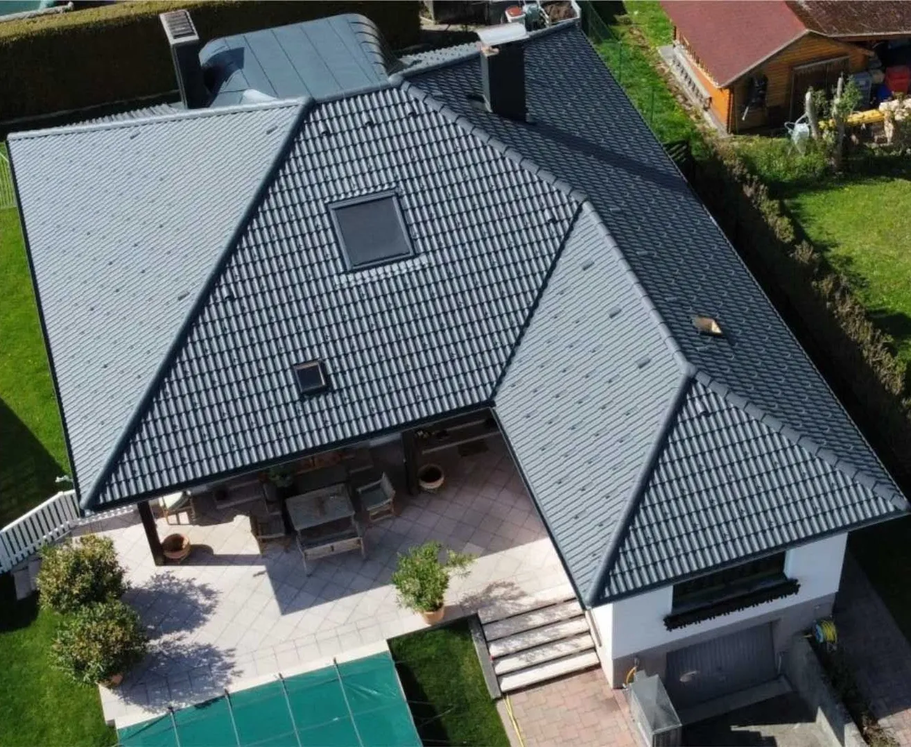 Ein Luftbild eines Hauses mit grauem Dach und einer Terrasse mit Tisch und Stühlen. Das Haus hat einen Schornstein und ein Fenster.
