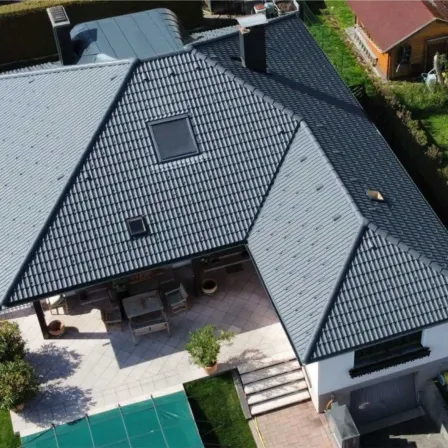 Ein Luftbild eines Hauses mit grauem Dach und einer Terrasse mit Tisch und Stühlen. Das Haus hat einen Schornstein und ein Fenster.
