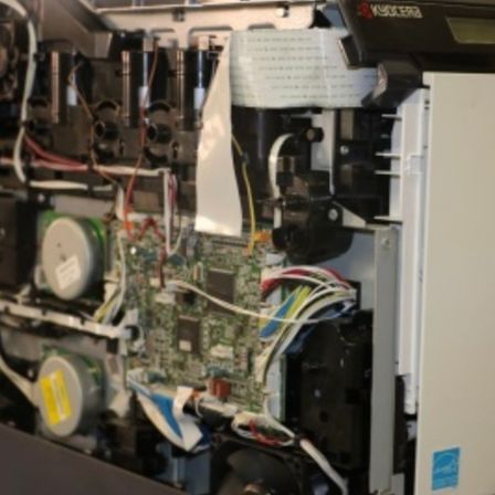 Das Innere eines Druckers zeigt seine internen Komponenten, einschließlich Zahnräder, Kabel und eine Leiterplatte, die zur Inspektion freigelegt sind.