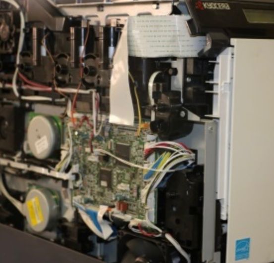 Das Innere eines Druckers zeigt seine internen Komponenten, einschließlich Zahnräder, Kabel und eine Leiterplatte, die zur Inspektion freigelegt sind.