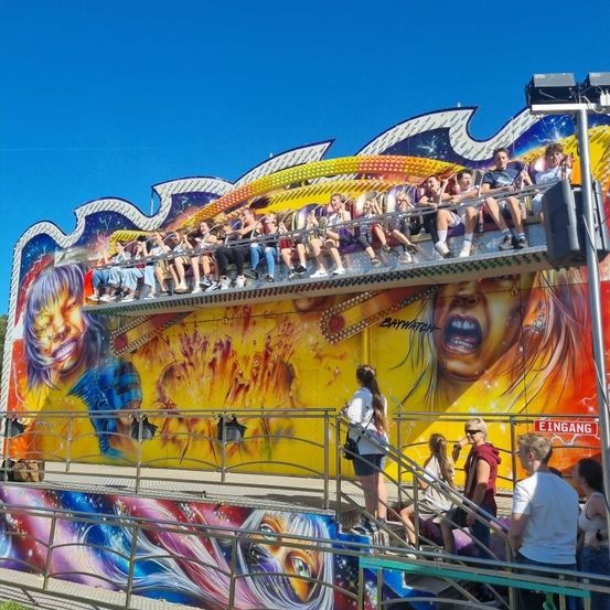 Eine bunte Fahrt mit Menschen, die darauf reiten, und anderen, die auf den Stufen stehen. Es ist unter einem blauen Himmel.