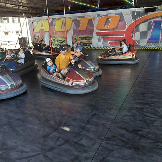 Eine Gruppe von Menschen, darunter Kinder und Erwachsene, genießen Bumper Cars in einem Vergnügungspark mit einem großen AUTO-Schild im Hintergrund.
