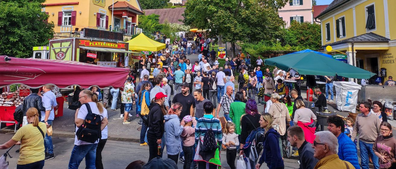 Eine Menschenmenge versammelt sich auf einem Stadtplatz, mit Imbissständen und einer Kirche im Hintergrund.
