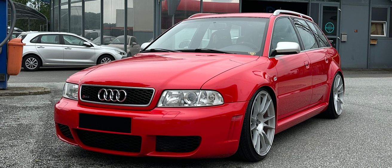Ein roter Audi RS4 steht vor einem Gebäude mit dem Schild 'Der Aubenreiten.at'. Hinter ihm sind weitere Autos geparkt.